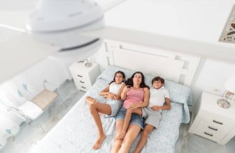 Família deitada na cama em um quarto claro e arejado, relaxando sob um ventilador de teto branco ligado.